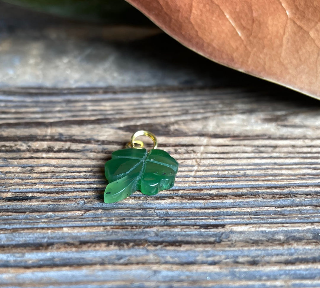 Single green shamrock charm with a gold bail on weathered wood