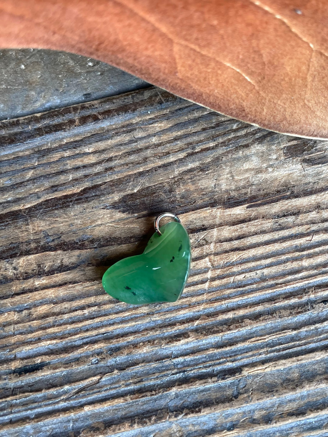 Single green jade heart charm with a metal loop on a weathered wooden surface.