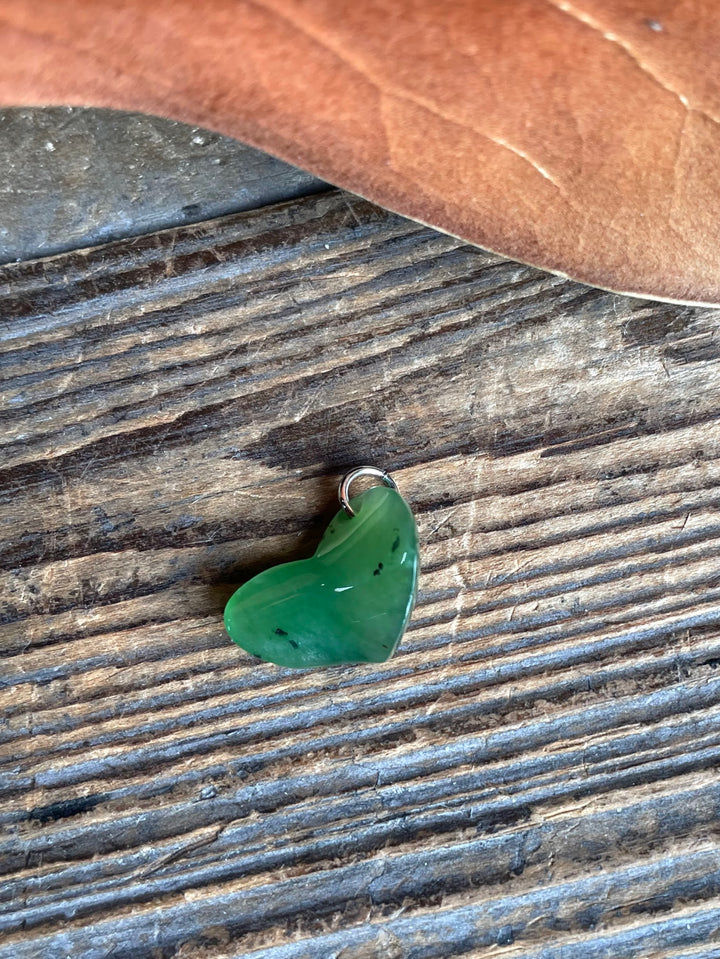 Single green jade heart charm with a metal loop on a weathered wooden surface.