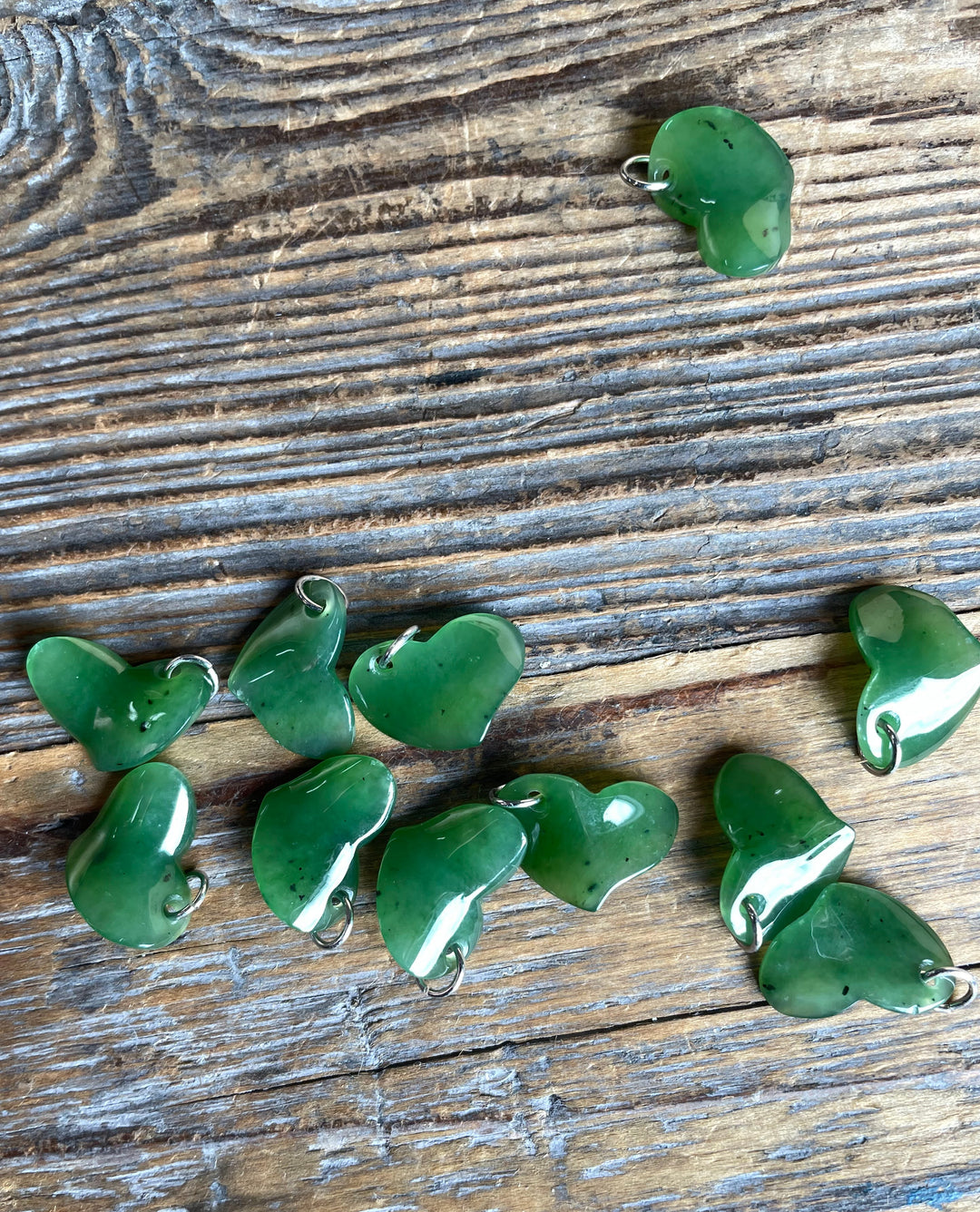 Green jade heart charms scattered across a rustic wooden surface
