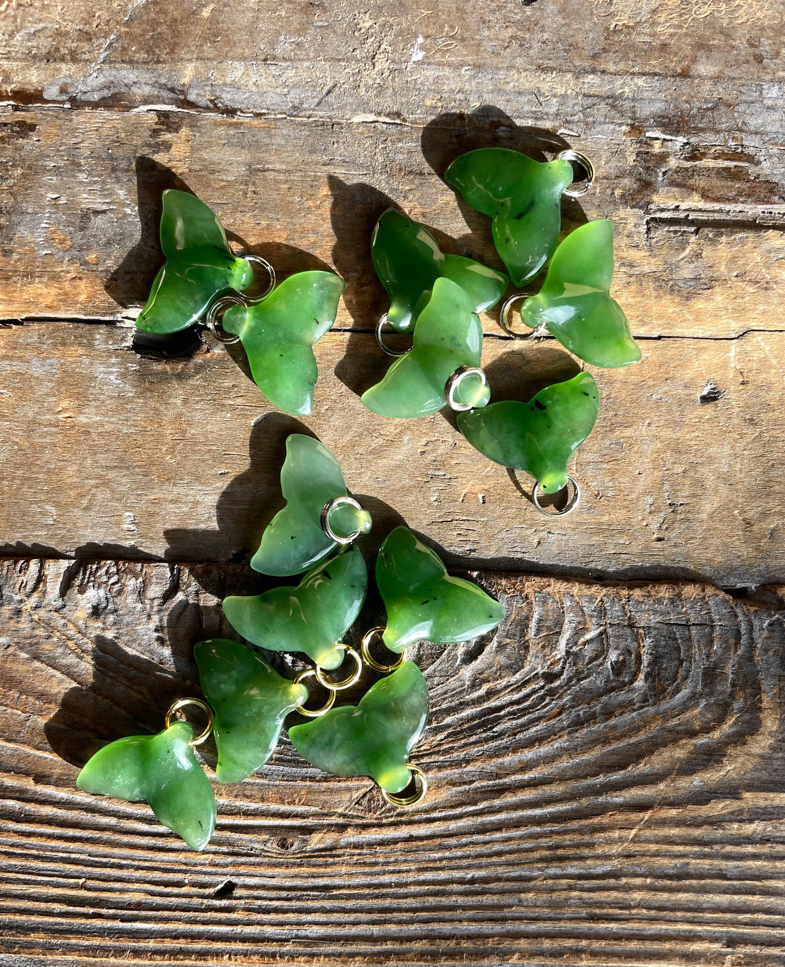 Group of green translucent whale tail charms with silver loops on a weathered wooden surface.