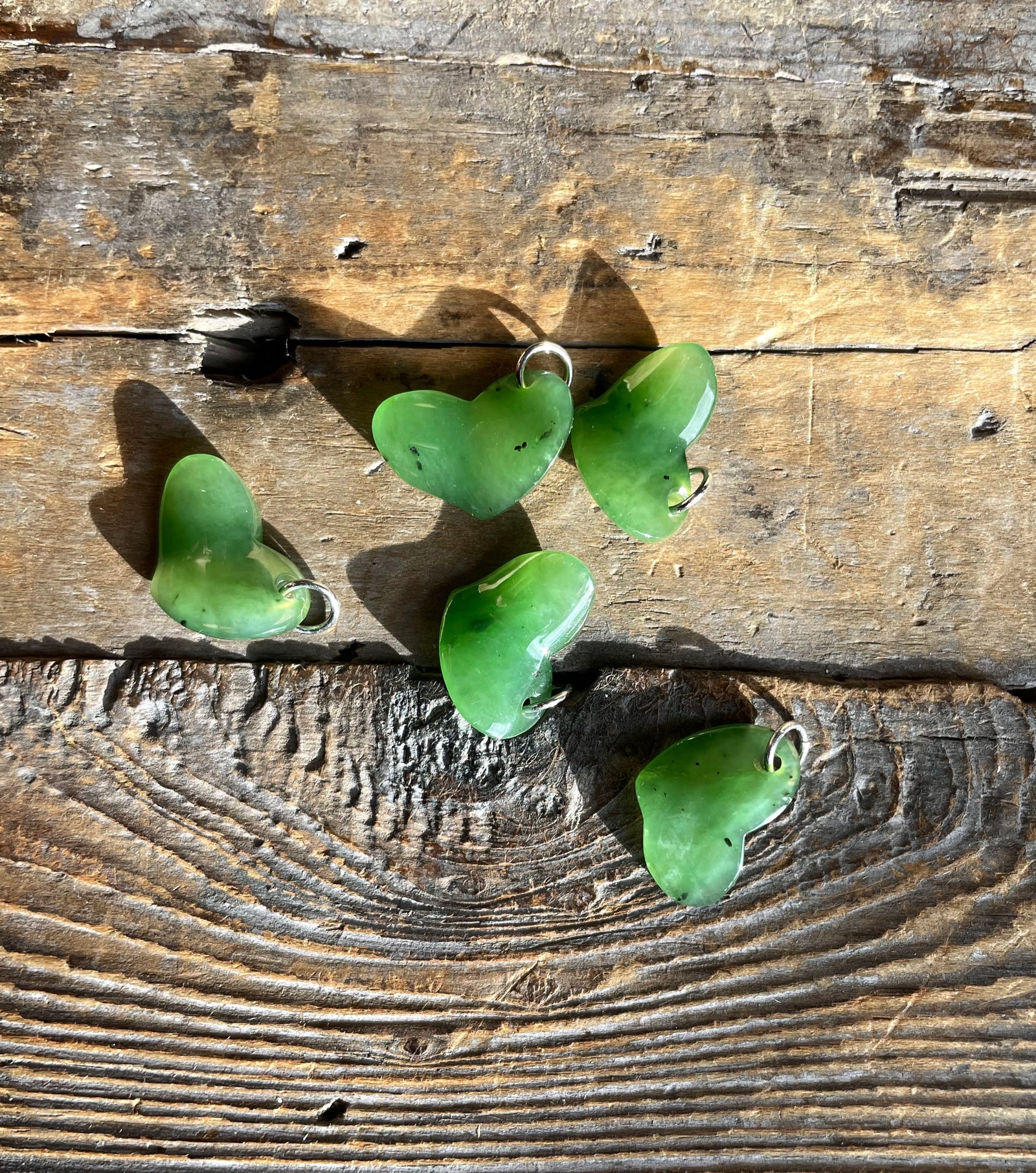 Green jade heart charms with metal loops scattered on a rustic wooden surface.