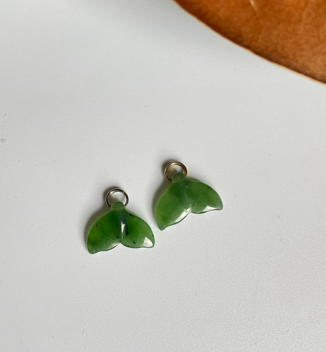 Two green whale tail charms with loops on a white background.