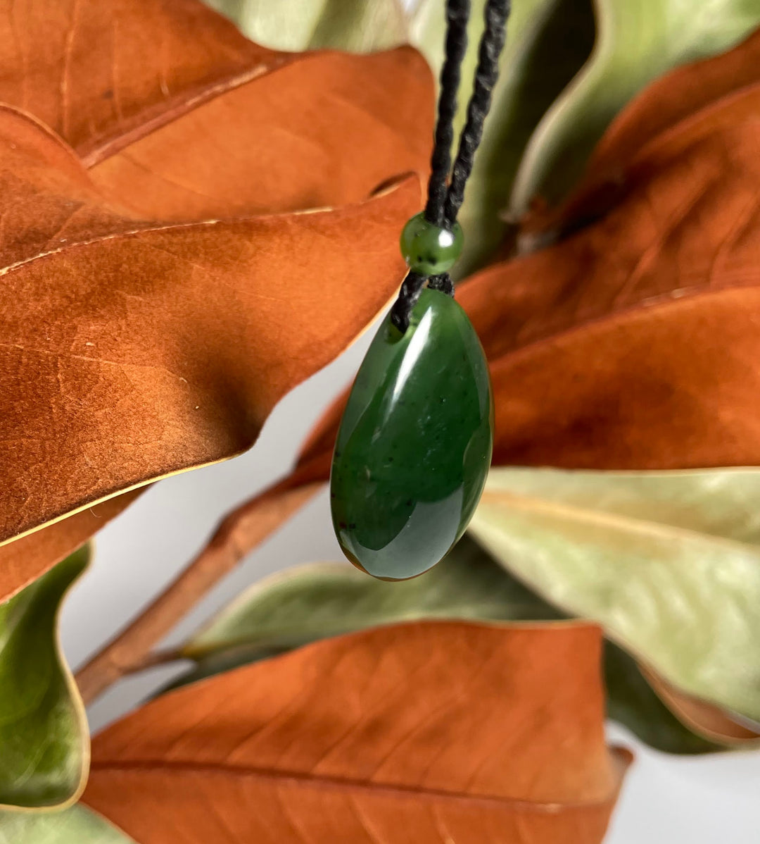 Close up of Jade teardrop pendant 23x32mm on a black cord with a green spacer bead against autumn leaves