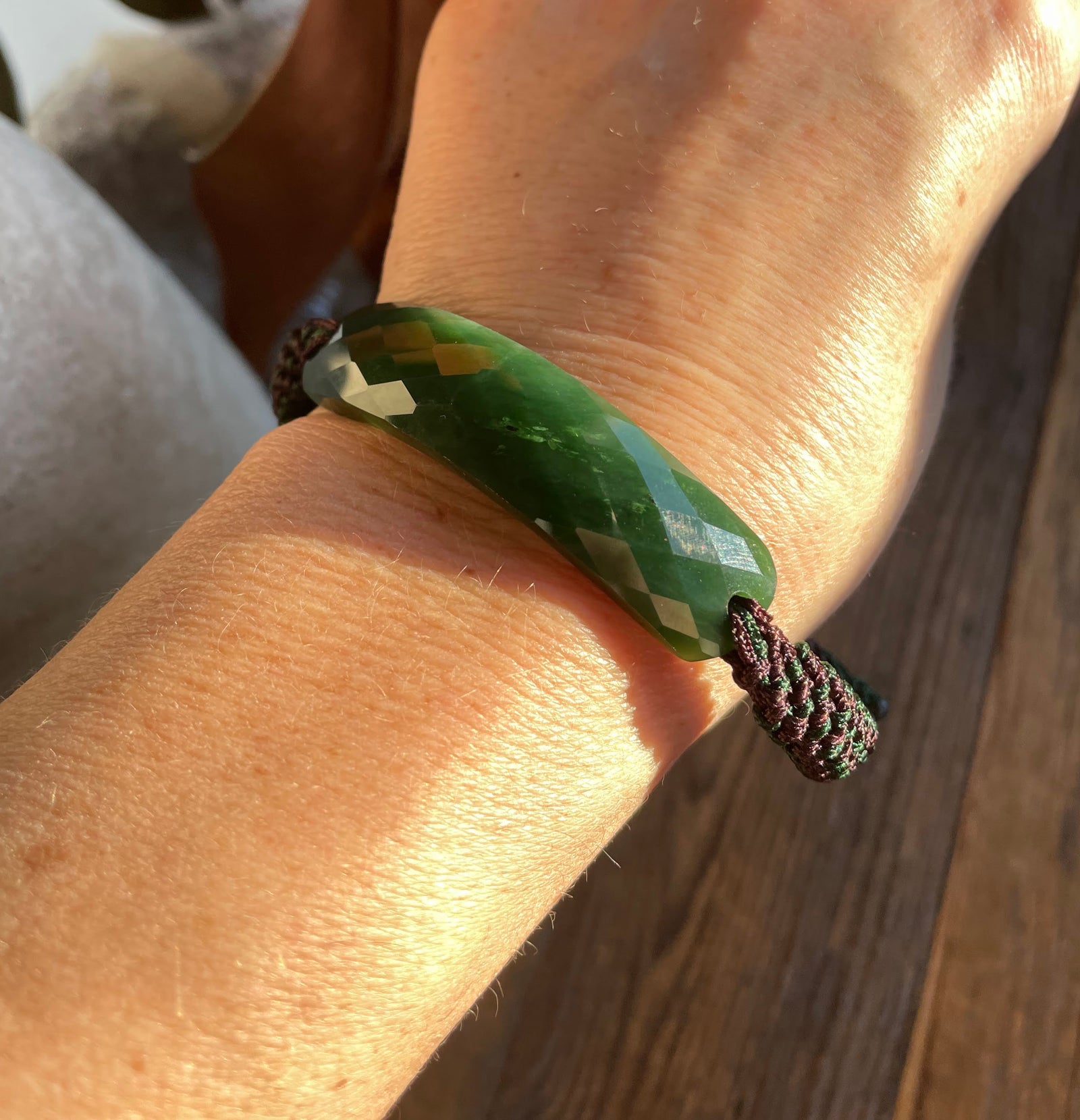 Green jade faceted bracelet on a wrist tied with a burgundy braided cord.