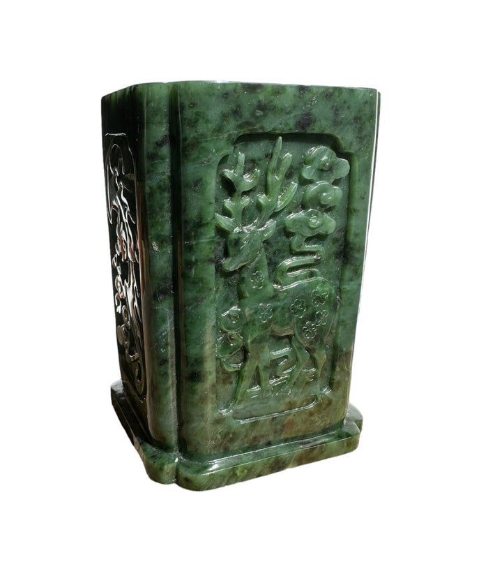Green jade vase pen holder shown from angle with a carved floral scene on the front panel and a side motif