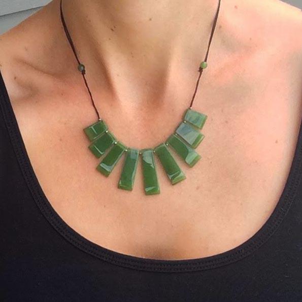Jade necklace with green rectangular beads on a black cord worn around the neck.