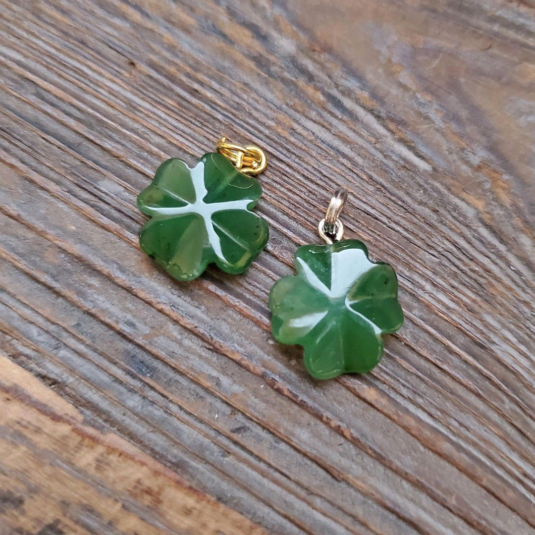 Green jade four leaf clover charms with white vein patterns and metal bails on wood grain.