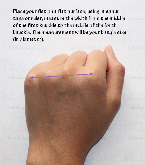 Hand demonstrates measuring bracelet size with a ruler to determine bangle diameter.