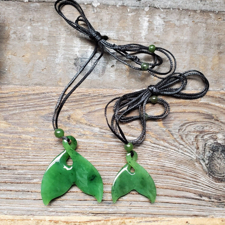 Pair of green whale tail pendants on black cords with green beads on wood background