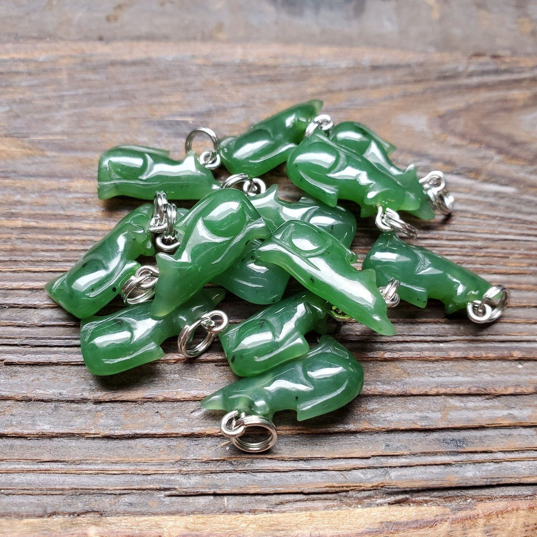 Pile of green jade wolf charms with silver loops on a wooden surface