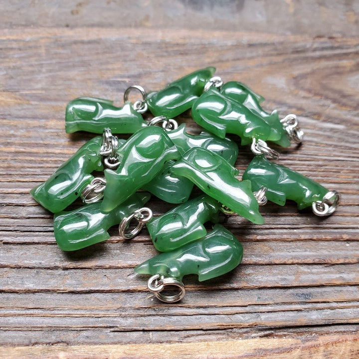 Pile of green jade wolf charms with silver loops on a wooden surface