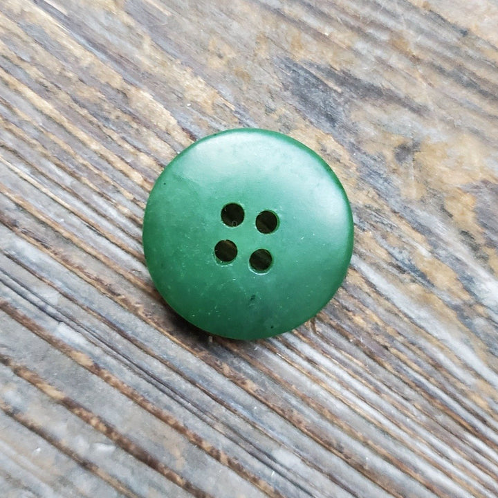 Top-down view of a green jade button with four holes on a textured wooden surface