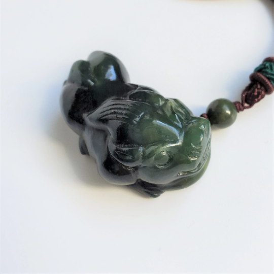 Dark green jade Pi Xiu pendant with cord and bead on a white background