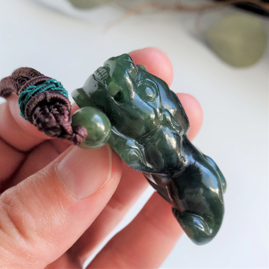 Close up of dark green jade Pi Xiu pendant on cord with a green bead