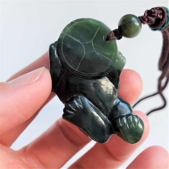Dark green jade Pi Xiu pendant on a brown cord held between fingers