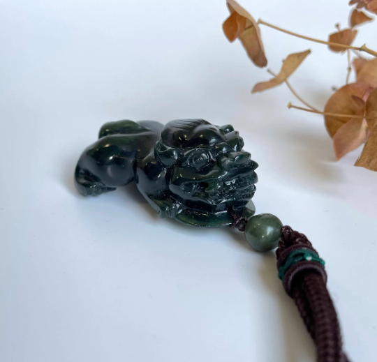 Dark green jade Pi Xiu pendant with brown cord and green bead.