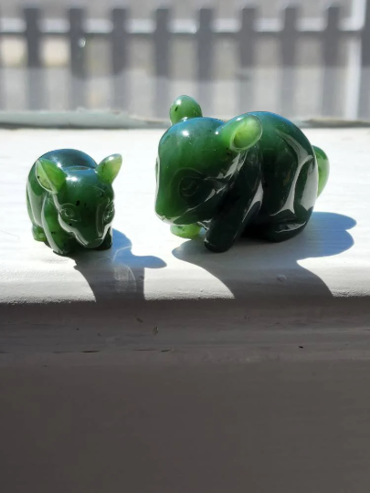 Pair of green jade chinchilla figurines in bright sunlight on a window ledge, small and large.