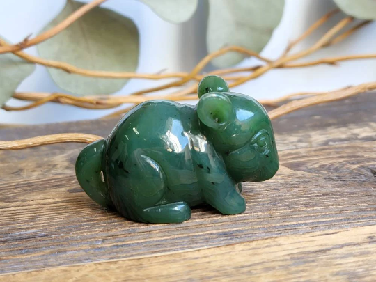 Green jade chinchilla figurine handcrafted and polished on a rustic wooden surface.