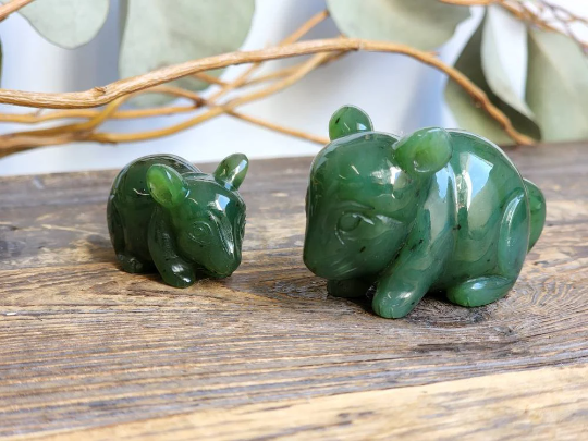 Two jade chinchilla figurines in dark green on a wooden surface