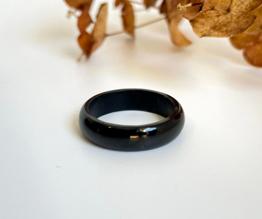 Close-up of a glossy black jade ring resting on a white surface with a dried plant in the background.