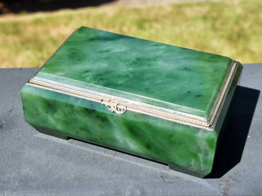 Green Siberian jade box with silver ornate edge trim and clasp, lid closed on a dark surface.