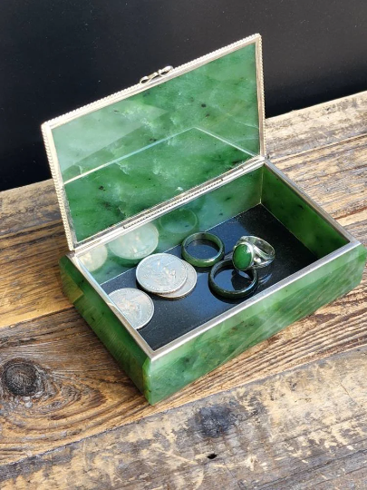 Open Siberian jade box with silver trim containing coins and rings inside on a dark lining.