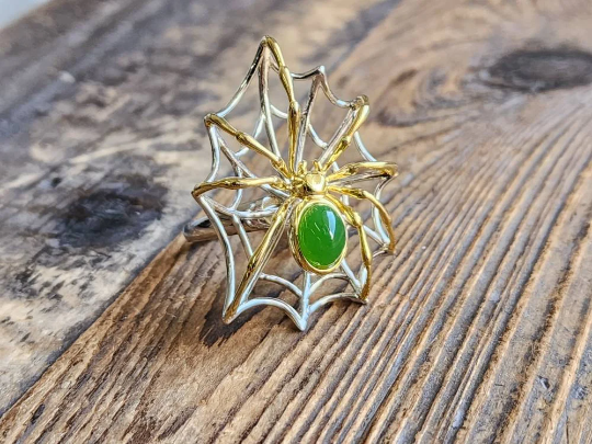 AA Spider Jade Ring with a green jade cabochon set in gold and sterling silver on a rustic wood surface