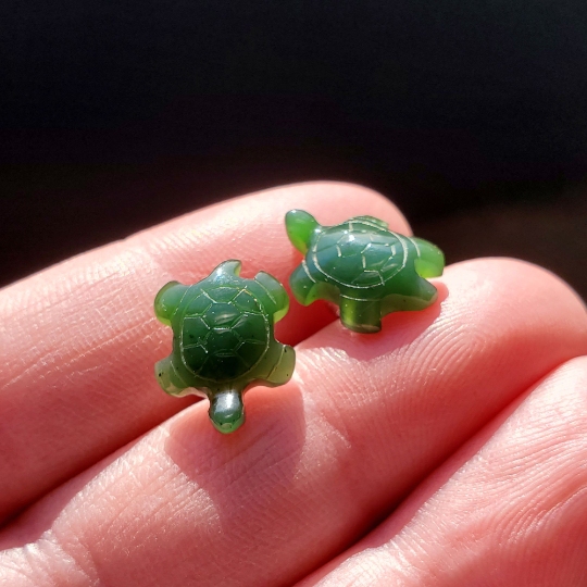 Two green turtle earrings held between fingers