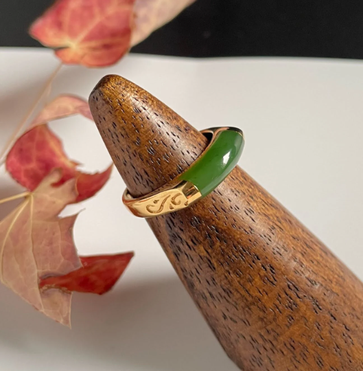 Green jade ring with a gold engraved band displayed on a wooden cone.