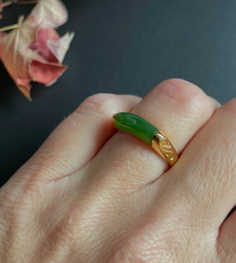 Green jade ring with a gold engraved band worn on a finger in a close-up.