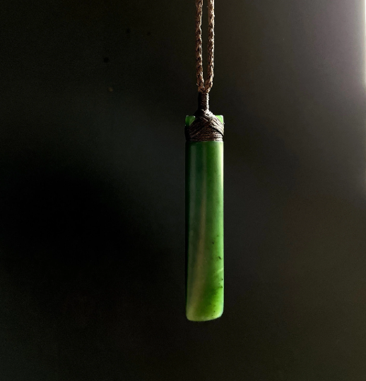 Green jade cylindrical pendant wrapped with cord against a dark background.