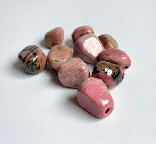 Pink polished rhodonite nuggets with dark veining scattered on a white background.