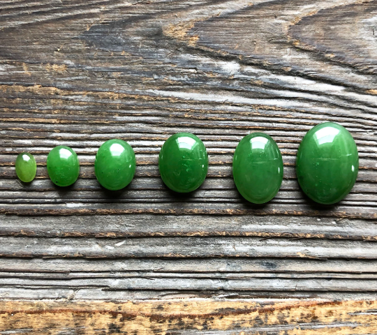 Five green oval cabochons in ascending size lined up on a weathered wooden surface