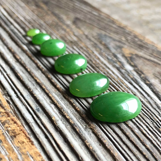 Green oval cabochons arranged in a line on a weathered wood surface with a ruler in the foreground