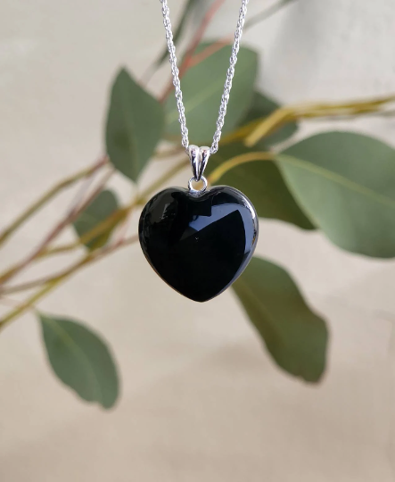 Heart shaped Australian black jade pendant on a silver chain against a leafy background