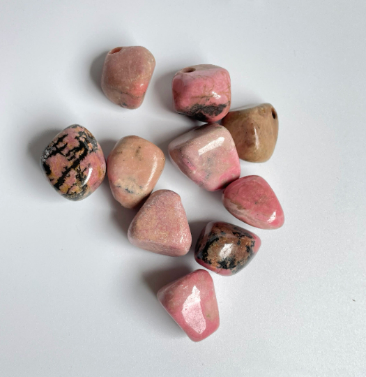 Pink rhodonite nuggets with dark veining arranged on a white background