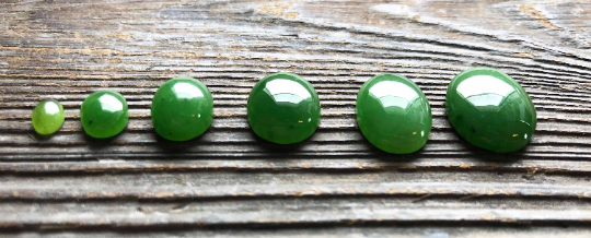 Row of green oval cabochon stones arranged from smallest to largest on a weathered wooden surface.