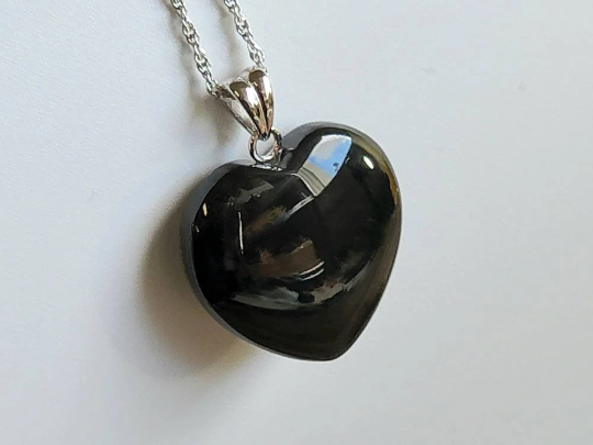 Heart shaped black jade pendant on a silver chain resting on a white surface