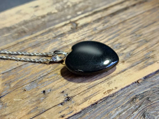 Australian black jade heart pendant on a silver chain resting on a wooden surface