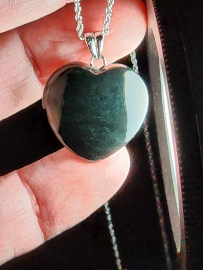 Heart shaped black jade pendant held between fingers with a silver bail and chain