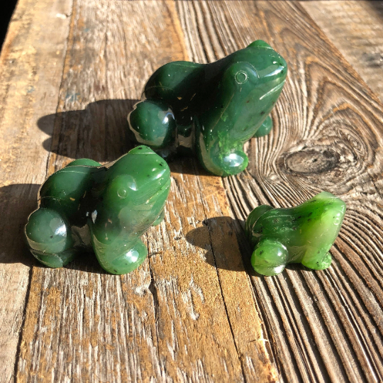 Three glossy green frog figurines of different sizes on a sunlit wooden surface