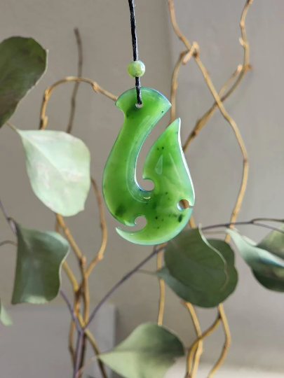 Canadian nephrite jade fish hook pendant in bright green hanging from a black cord.