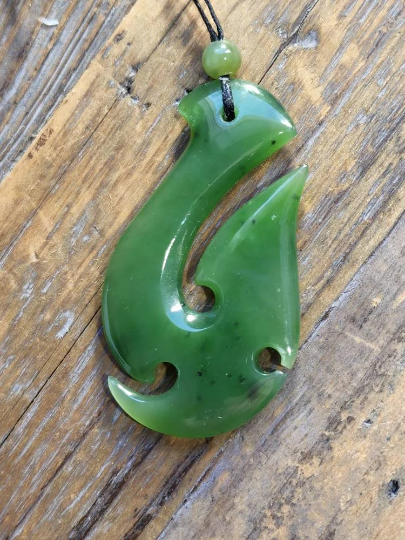 Green nephrite jade fish hook pendant on black cord with bead at the top