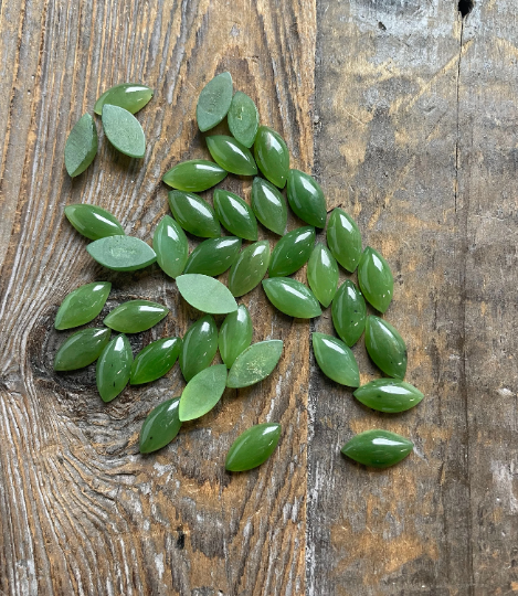Green nephrite jade navette cabochons scattered on a weathered wooden surface