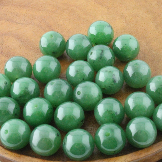 Group of glossy green 12mm Canadian jade beads in a wooden dish