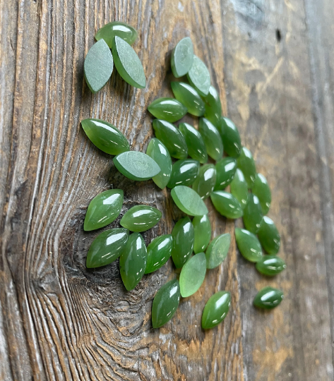 Assorted nephrite jade navette cabochons in varying sizes scattered on a rustic wooden surface