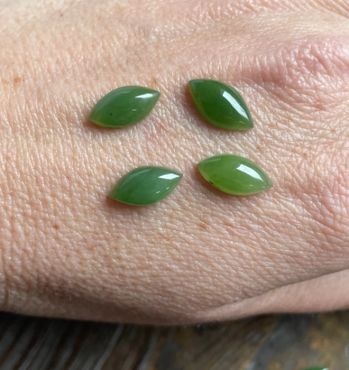 Four glossy green nephrite jade navette cabochons on skin, arranged in a loose square.