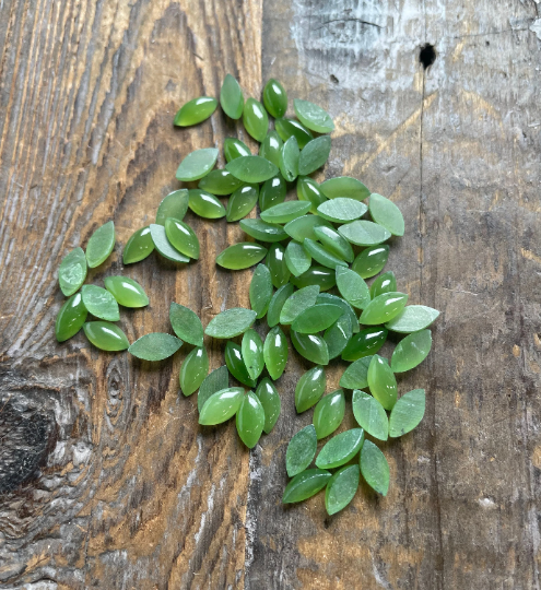 Assorted small green nephrite jade navette cabochons scattered on a rustic wooden surface