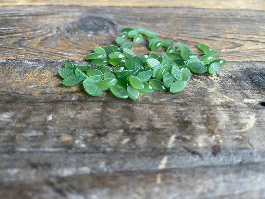 Cluster of small green nephrite jade navette cabochons scattered on a weathered wooden surface.